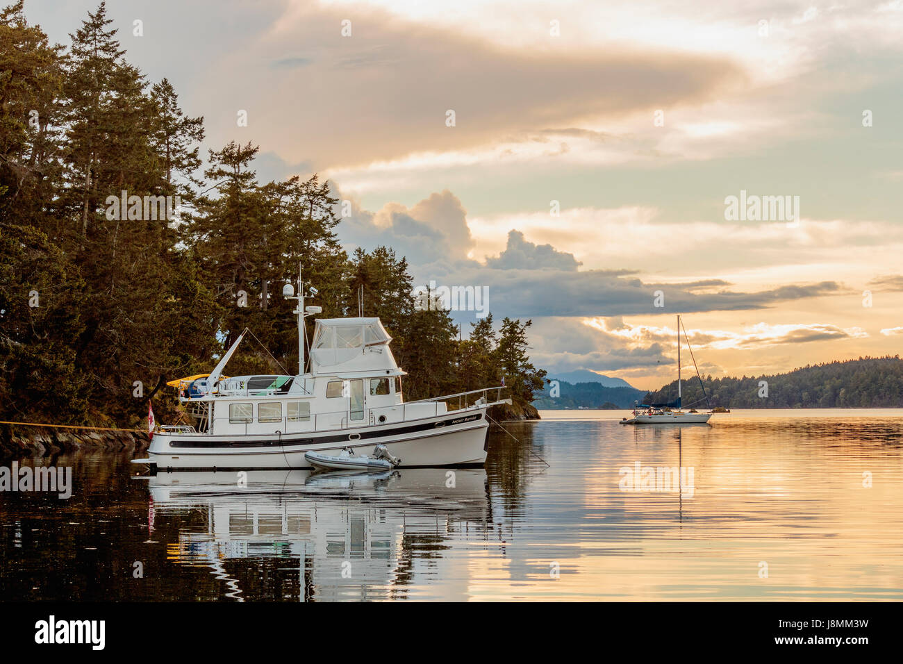 Zwei Boote (a Nordic Tug und ein Segelboot) sind bei Sonnenuntergang auf einem ruhigen Abend an einem Marine Park in British Columbia Gulf Islands verankert. Stockfoto