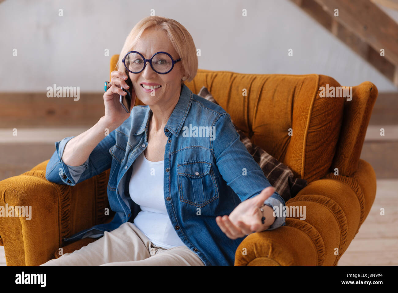 Ich bin ganz Ohr. Attraktive Reife Frauen tragen Runde Gläser und halten ihr Handy in der Nähe von rechten Ohr beim gestikulieren mit linken hand Stockfoto