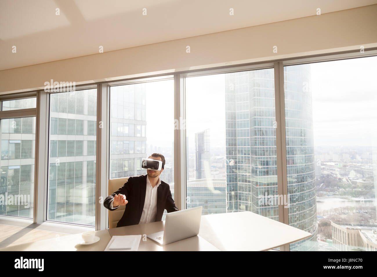 Mann am Schreibtisch in VR Kopfhörer zeigt auf die Luft Stockfoto