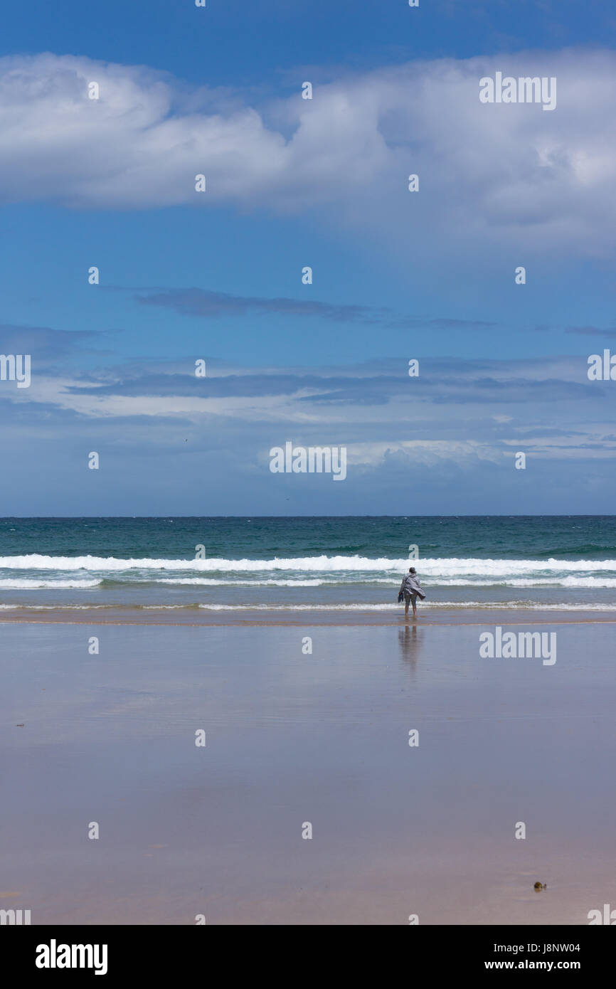 Eine Dame steht mit Blick auf die Wellen, die ans Ufer mit einer leichten Brise an einem frühen Frühlingstag mit blauem Himmel und leichte Wolken. Stockfoto