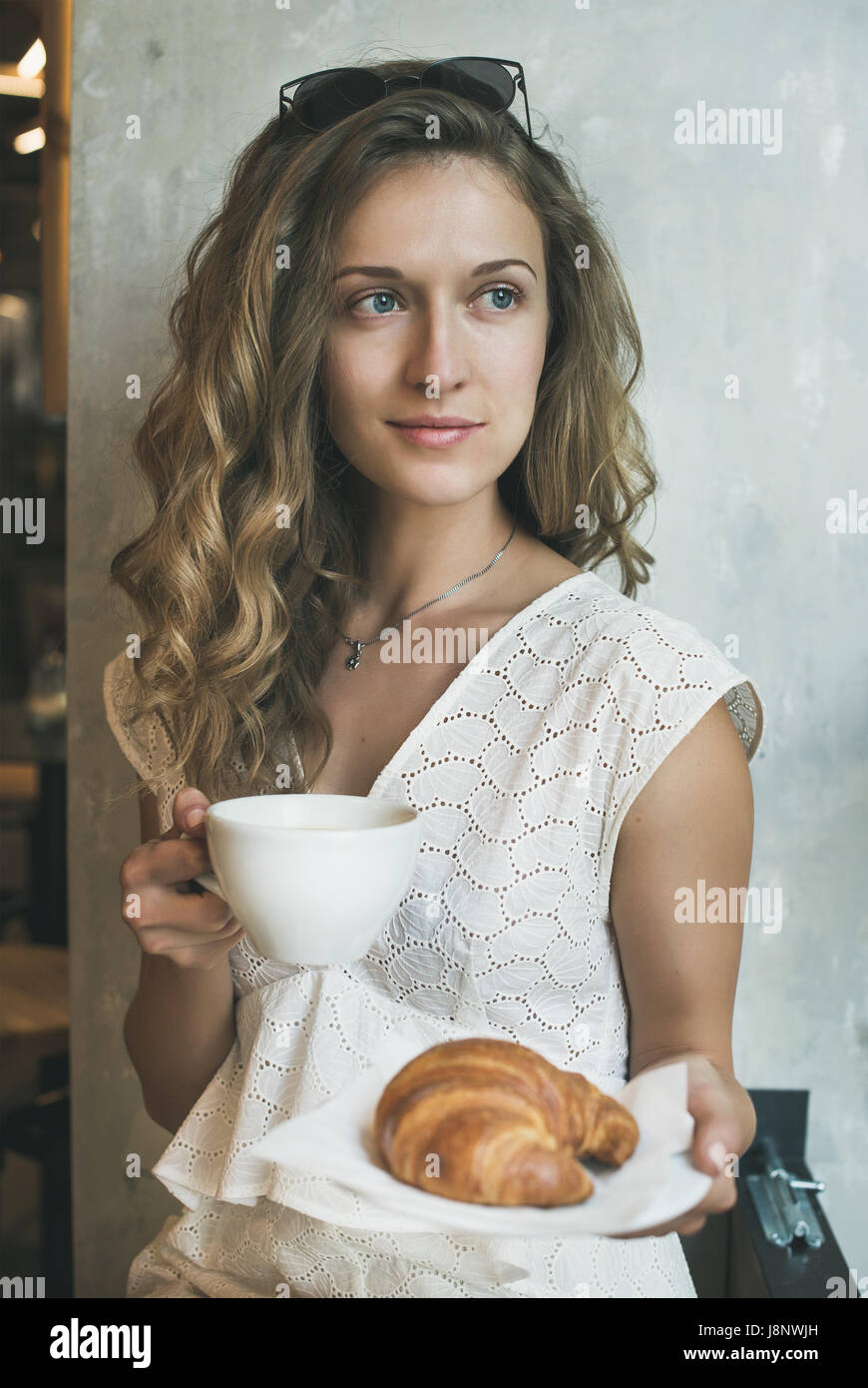 Blonde Frau sitzt mit Tasse Cappuccino und croissant Stockfoto