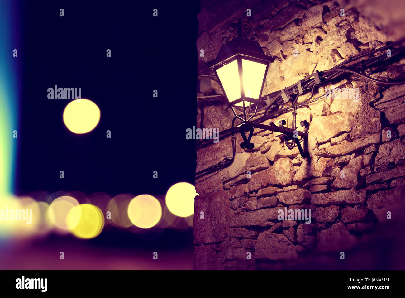 Lichter der Stadt und Laternenpfahl in der Fassade. Steinmauer Hintergrund bei Nacht Stockfoto