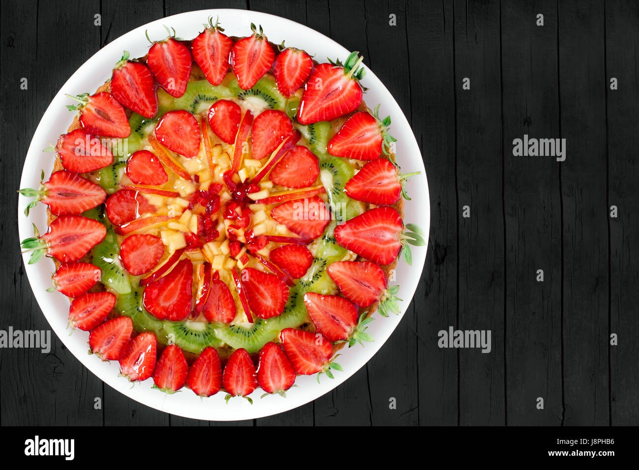 Frisches Obst-Torte mit Erdbeeren, Pfirsiche und Kiwi, auf schwarzem Holz Hintergrund, Ansicht von oben geschossen mit textfreiraum verziert. Stockfoto