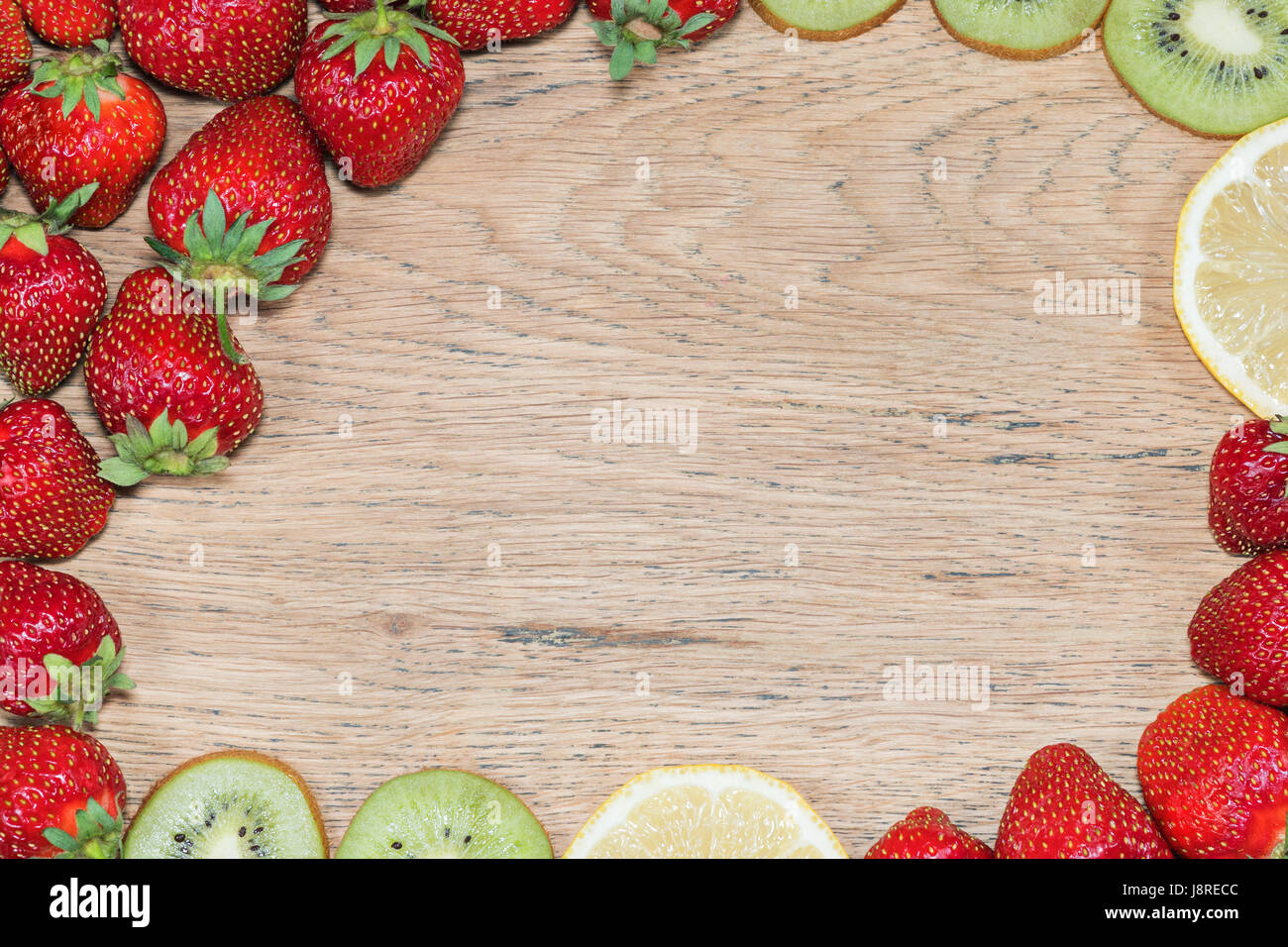Hölzerne Struktur mit Erdbeeren, Kiwi und Zitronenscheiben verteilt an den Rändern wie ein Rahmen Stockfoto