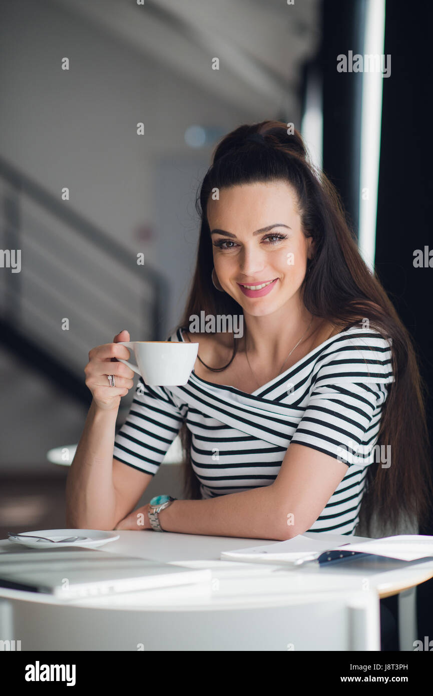 Porträt einer charmanten Frau am Tisch sitzen und eine Tasse Tee, schaut in die Kamera halten. Stockfoto