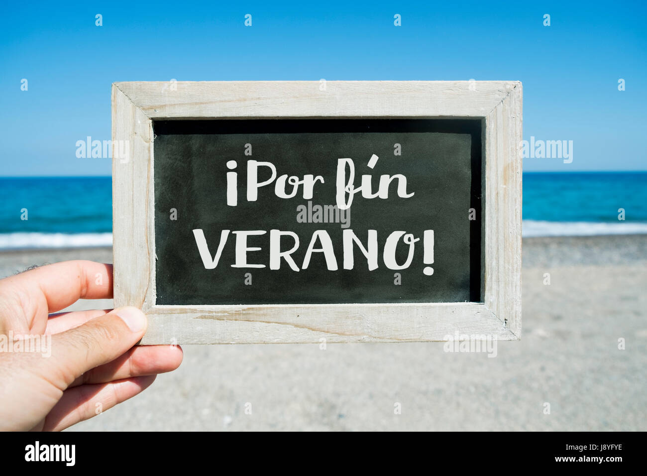 Nahaufnahme der Hand von einem kaukasischen Jüngling hält eine Tafel mit dem Text Por Fin Verano, endlich Sommer in Spanisch geschrieben, am Strand, Stockfoto