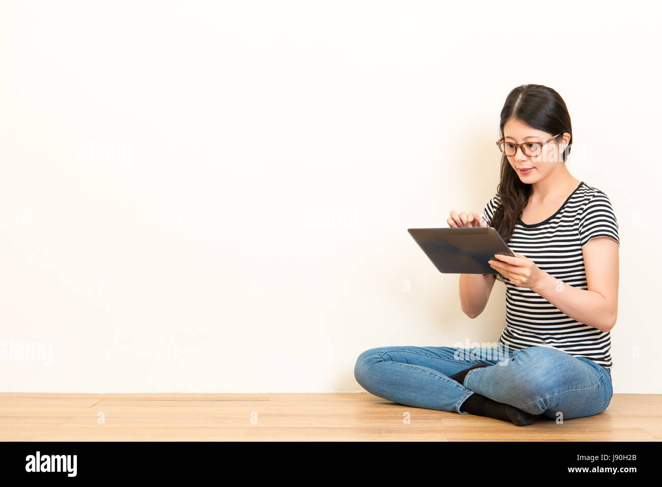 Ernst sitzen junge Dame mit Pad und Notenschreiben suchen etwas auf Holzboden über leere Kopie Raum weiße Wand Hintergrund. Stockfoto