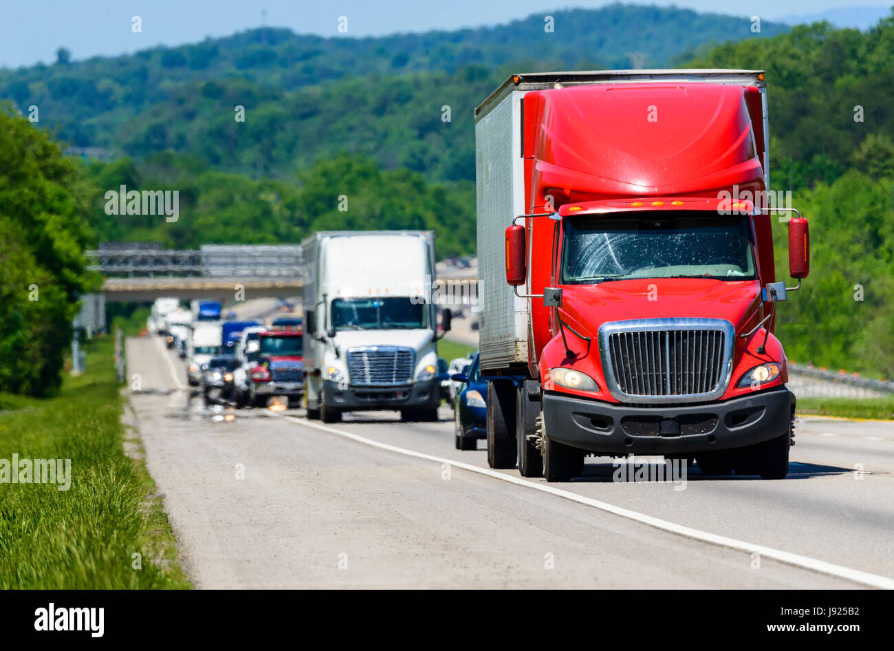 Eine rote Semi führt eine Reihe von Verkehr auf einer Autobahn in Tennessee.  Wärme steigt vom Gehsteig gibt Hintergrund LKW und Wald eine coole s Stockfoto