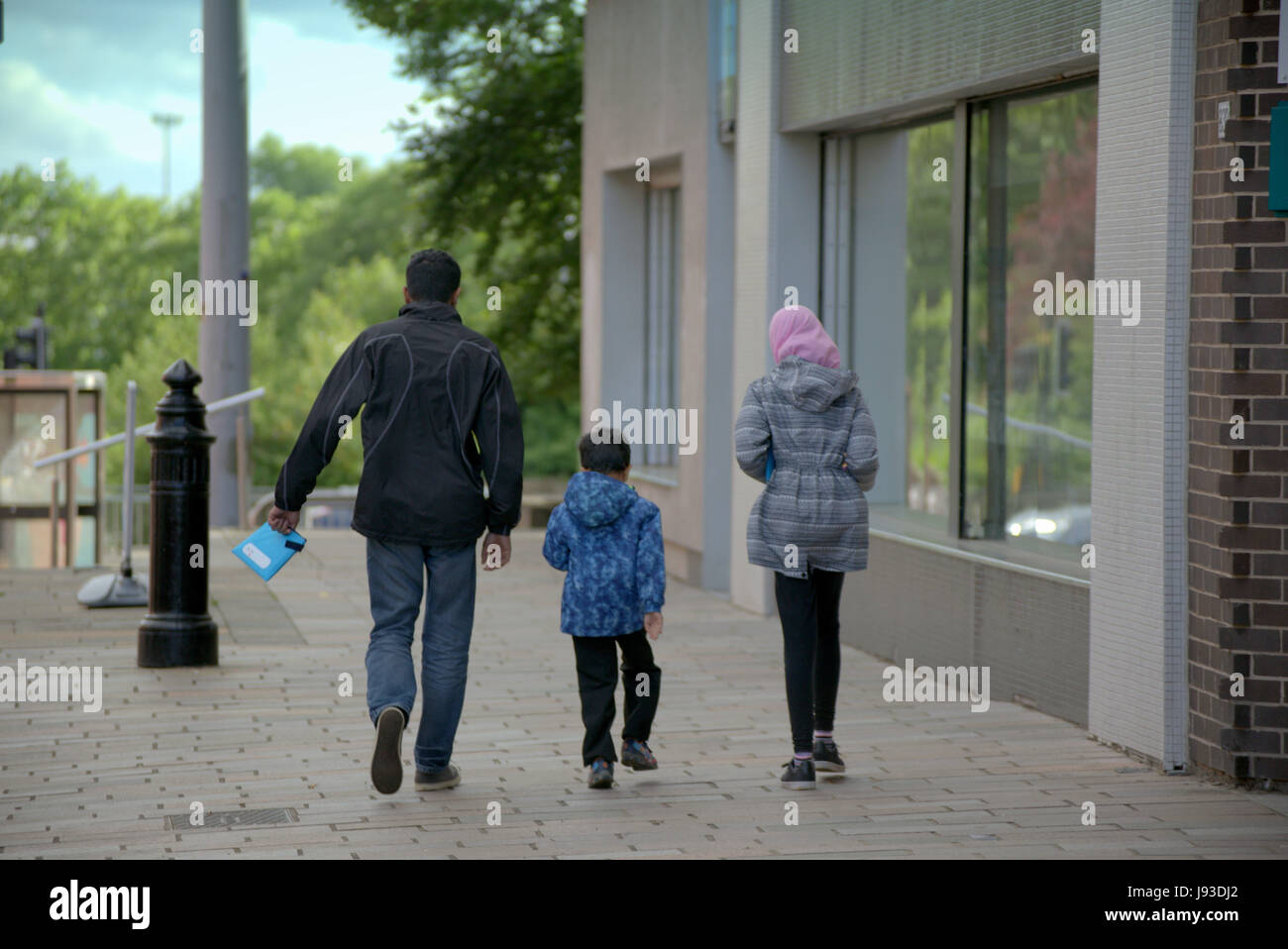 Asiatische Familie Schwarz Flüchtling Hijab Schal auf Straße in der UK alltägliche Szene in hand gehen mit Formen gekleidet Stockfoto