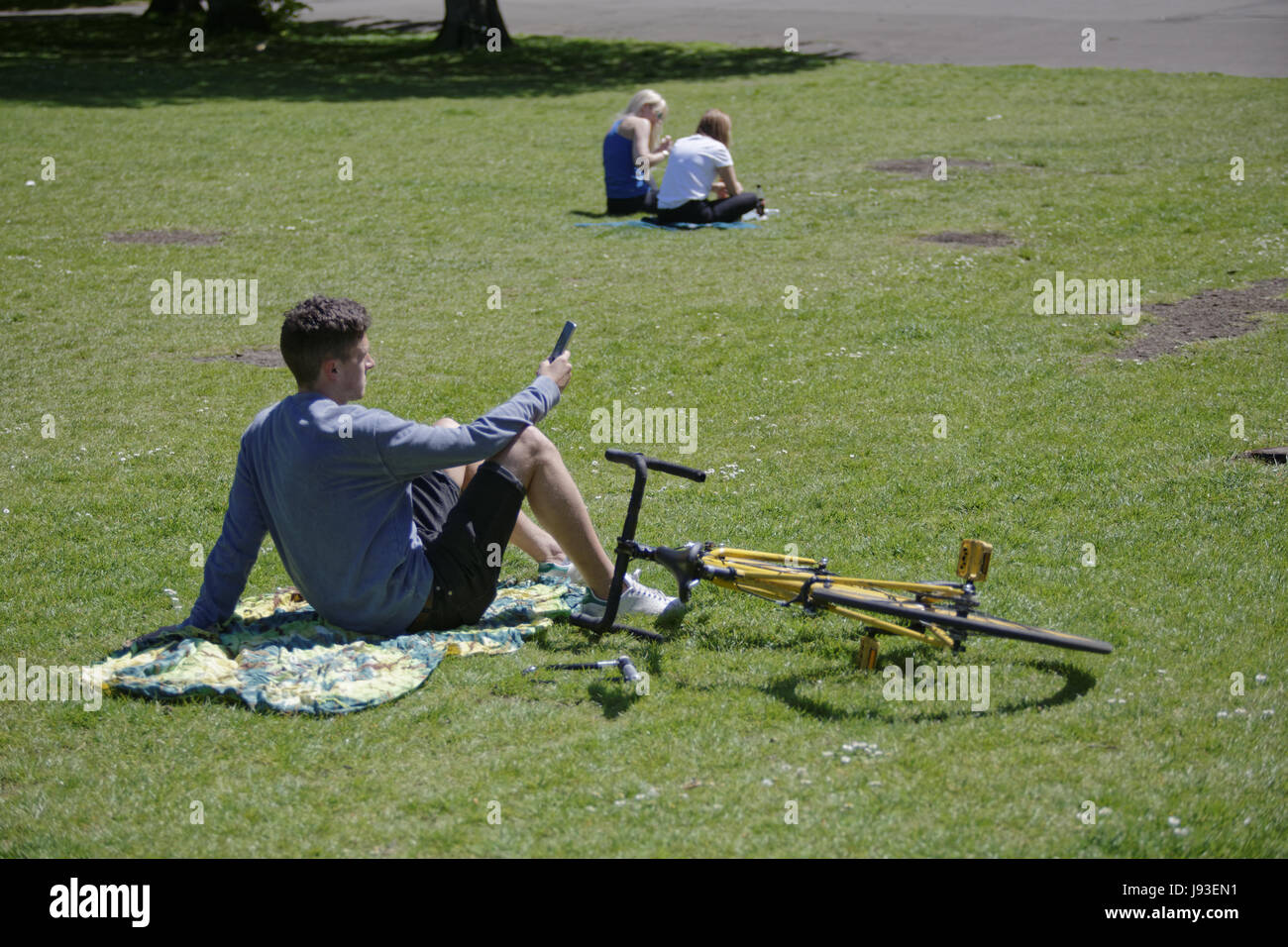 Glasgower heraus in die Grünflächen der Kelvingrove Park als die Temperaturen stiegen für den zweiten Tag in ein Zeile junge mit smart Handy-Mädchen Stockfoto