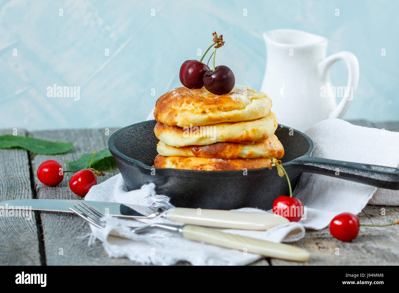 Hausgemachter Hüttenkäse Pfannkuchen mit Kirschen in einer gusseisernen Pfanne. Russische Dessert aus Quark. Stockfoto