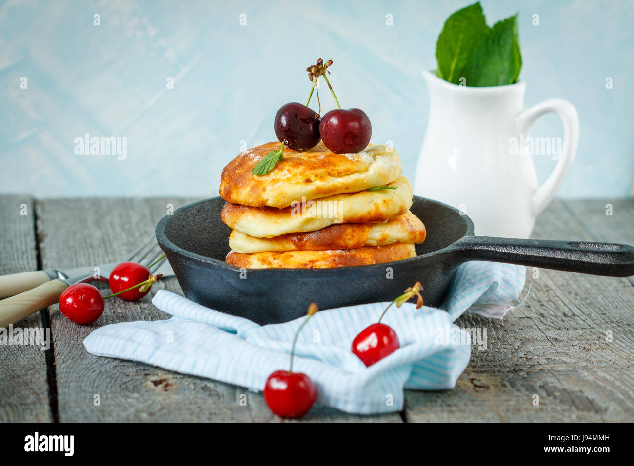 Hausgemachter Hüttenkäse Pfannkuchen mit Kirschen in einer gusseisernen Pfanne. Russische Dessert aus Quark. Stockfoto