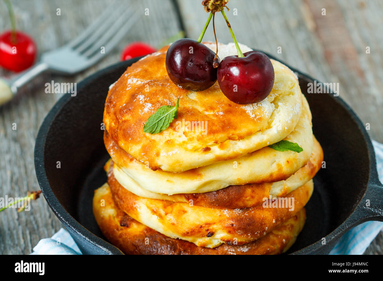 Hausgemachter Hüttenkäse Pfannkuchen mit Kirschen in einer gusseisernen Pfanne. Russische Dessert aus Quark. Stockfoto