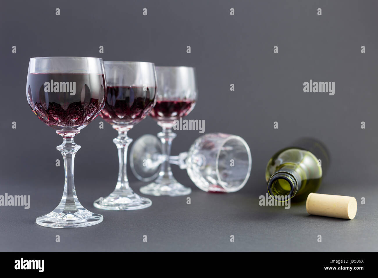 Konzept der Konsum von Alkohol, Alkoholismus und Missbrauch mit einer Reihe von schöne Kristallgläser mit Rotwein und eine leere Flasche gefüllt. Stockfoto