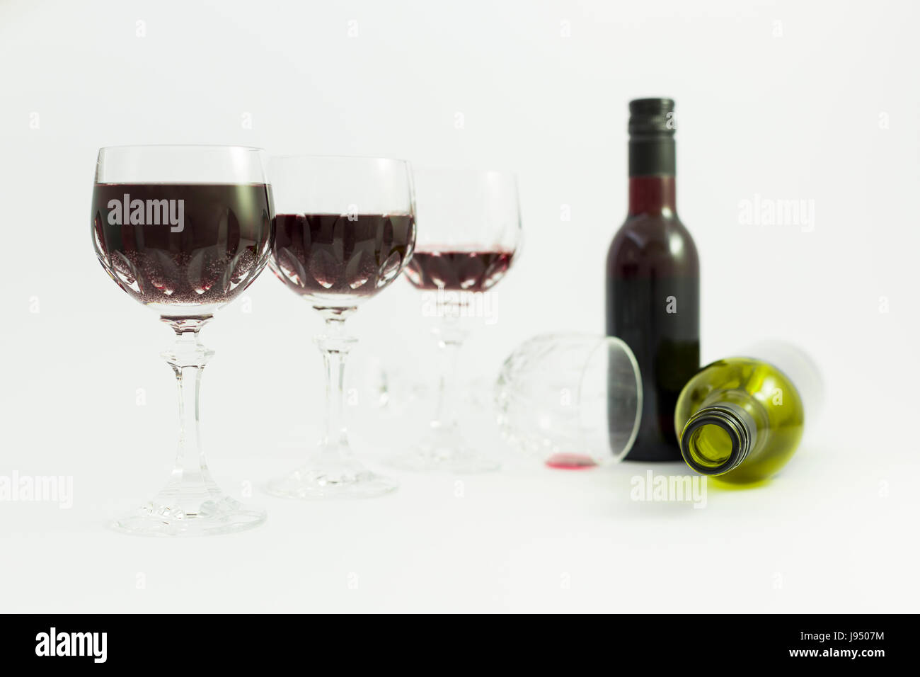 Konzept der Konsum von Alkohol, Alkoholismus und Missbrauch mit einer Reihe von schöne Kristallgläser mit Rotwein, eine volle und eine leere Flasche gefüllt. Stockfoto