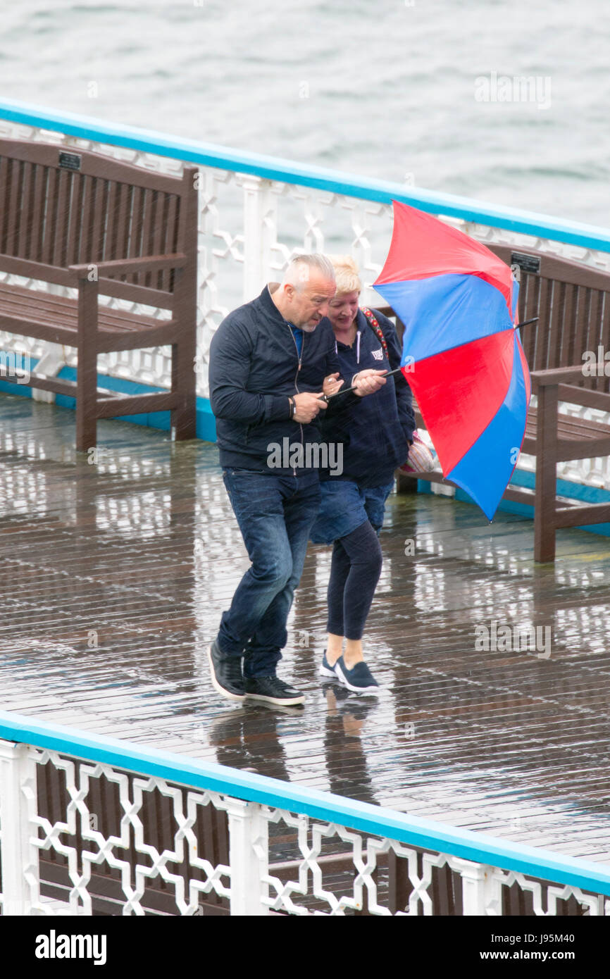 Ein paar Auseinandersetzung mit ihren bunten Regenschirm zum Schutz vor der nassen und windigen Wetter auf dem Holzsteg von Llandudno Pier in der touristischen Stadt von Llandudno, Nordwales Stockfoto