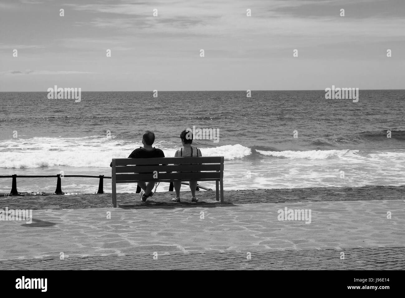 Urlaub paar sitzen und entspannen auf einer Holzbank, wie sie in den Atlantischen Ozean von der Promenade am Playa Las Americas in Teneriffa in th aussehen Stockfoto