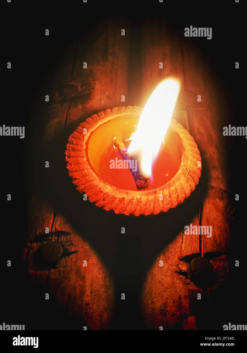 Flamme Licht auf kleine Keramik Kerze Basis. Es hat auf Holzboden im dunklen Bereich mit abstrakten Bokeh hellen Hintergrund unscharf gestellt. Stockfoto