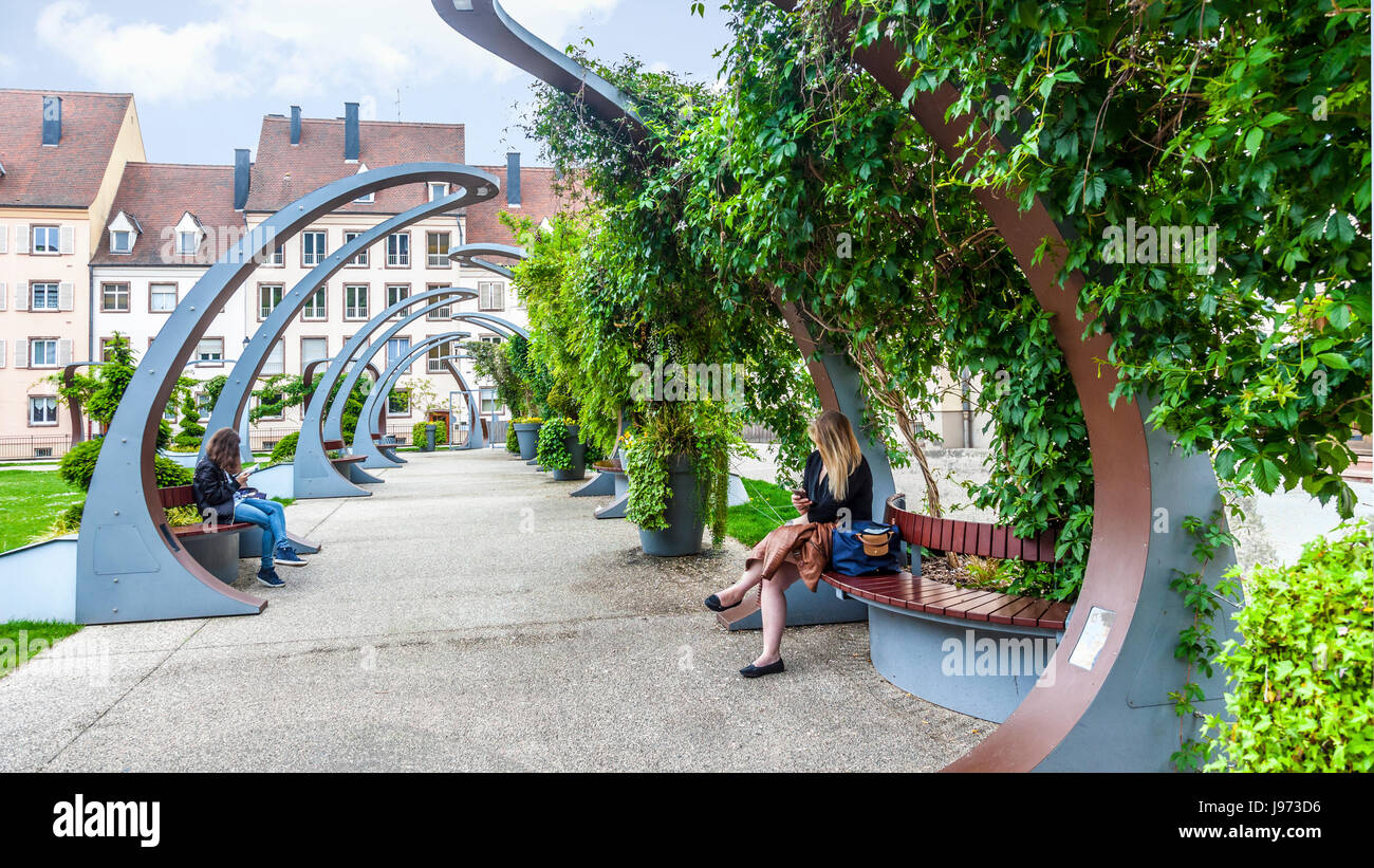 Zwei junge Frauen, die zum Entspannen in der grünen Kreuzgang (2012) - Place du 2 Février, einem beliebten Platz im Zentrum von Colmar, Frankreich. Stadthäuser im Hintergrund Stockfoto