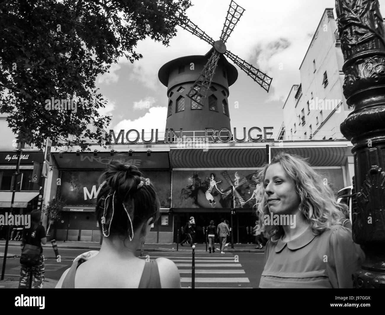 Zwei Frauen gehen in das Moulin Rouge in Paris, Frankreich.  Die Moulin-Rouge-Windmühle zu sehen. Stockfoto