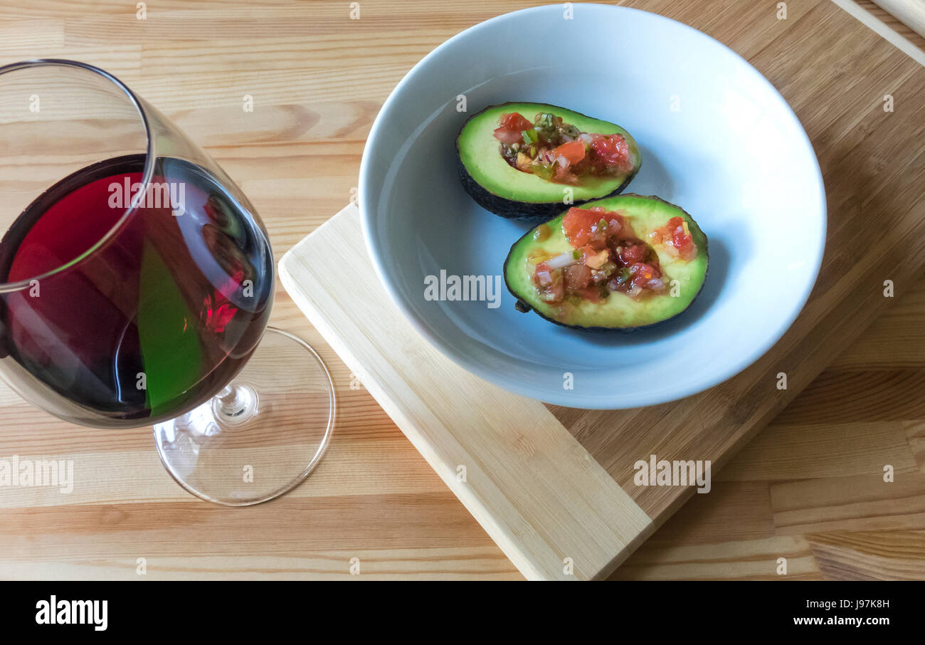 Eine Avocado und Salsa Fresca in einer weißen Schüssel mit einem Glas Rotwein Stockfoto