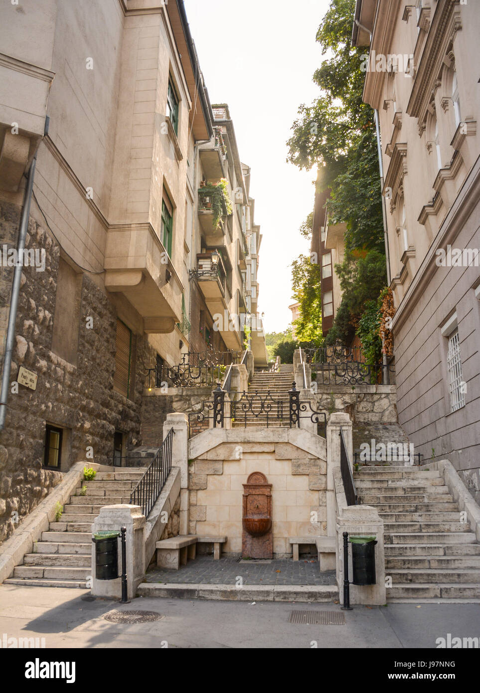 Blick durch eine schmale Straße mit historischen Gebäuden beider Seiten und Sonnenlicht am Ende. Ort: Budapest, Ungarn, Europa. Stockfoto