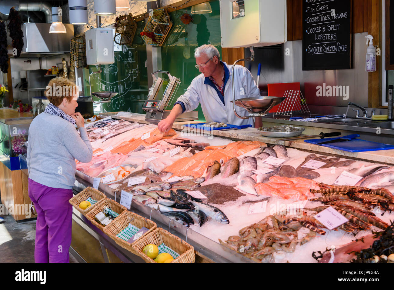 Ein Fischhändler hebt Fisch aus eine große Theke, bestückt mit viel frischem Fisch und Meeresfrüchten, Howth, Irland. Stockfoto