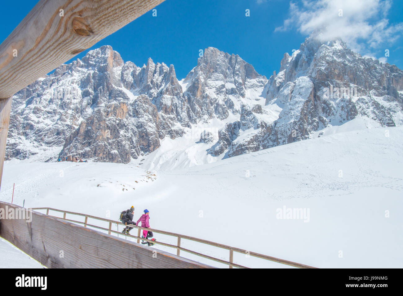 Zwei Wanderer Freunde betrachten die schönen Berge vor ihnen sitzen auf einem hölzernen Zaun und Einweichen in der Sonne, auf dem Schnee reflektiert. Stockfoto