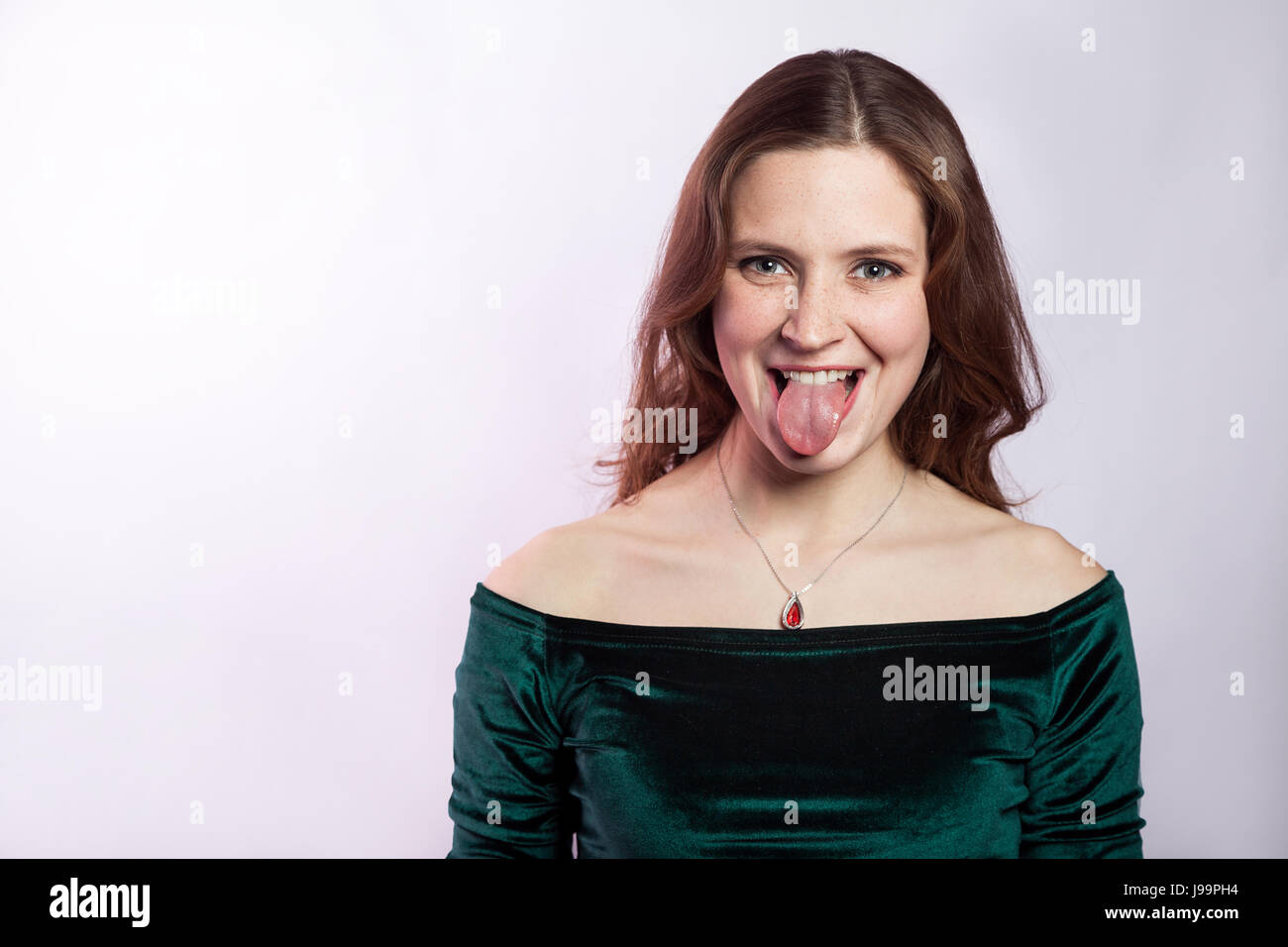 Porträt von lustige verrückte Frau mit Sommersprossen und klassischen grünen Kleid mit Zunge. Studio auf Silber grauen Hintergrund gedreht. Stockfoto