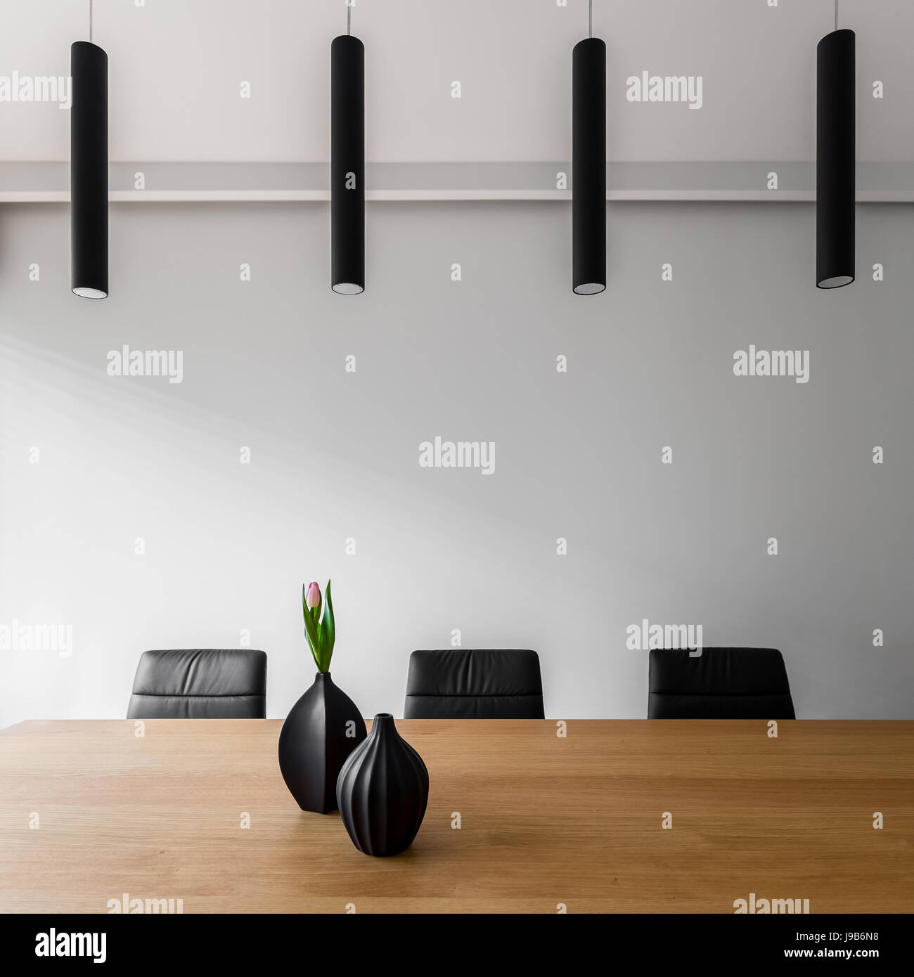 Weißer Raum mit Holztisch, schwarzen Stühlen und moderne Deckenleuchten Stockfoto