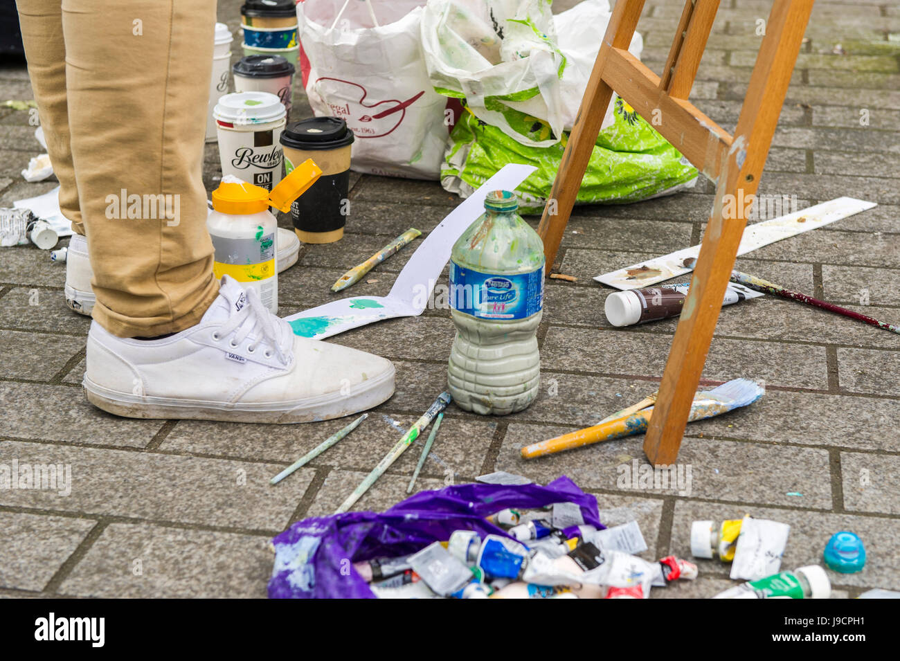 Farbe, Pinsel und Utensilien des Künstlers auf Asphalt wie ein Künstler eine Straßenszene auf der Grand Parade, Cork, Irland malt. Stockfoto