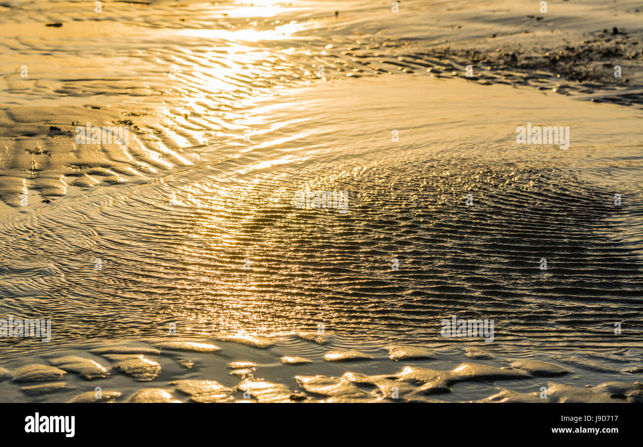 Wellen von Wasser bei Ebbe an einem Sandstrand mit Sonnenlicht reflektieren im Meerwasser. Stockfoto