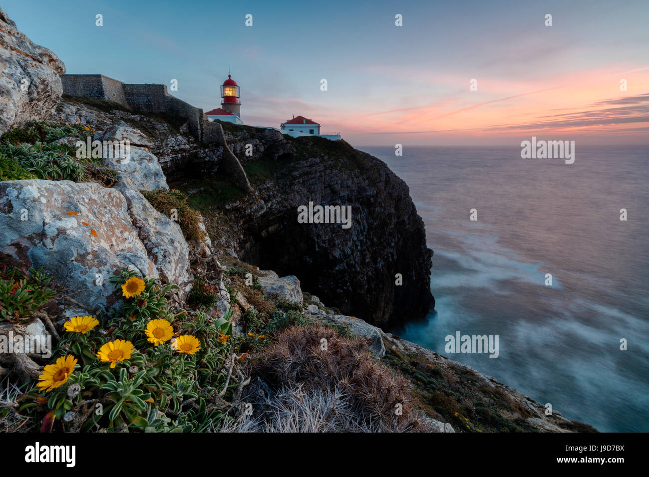 Rosa Himmel bei Sonnenuntergang und gelbe Blumen umrahmen den Leuchtturm Cabo De Sao Vicente, Sagres, Algarve, Portugal, Europa Stockfoto