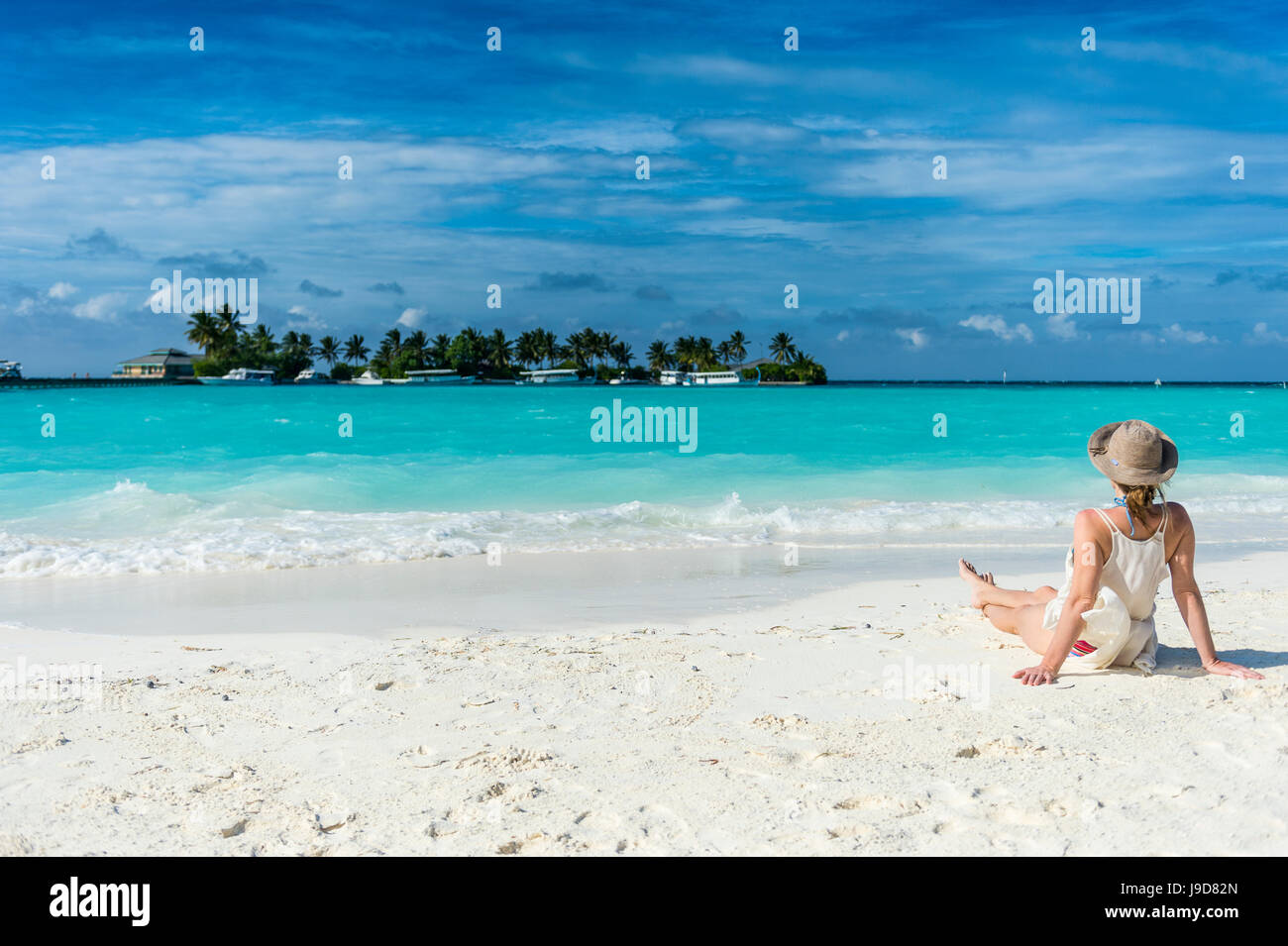 Frau sitzt auf einem weißen Sandstrand genießen das türkisfarbene Wasser, Sun Island Resort, Insel Nalaguraidhoo, Ari Atoll, Malediven Stockfoto