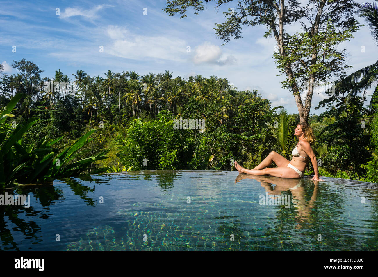 Frau genießen einen überlaufenden Pool über einem Tal im Kamandalu Ubud Resort, Ubud, Bali, Indonesien, Südostasien, Asien Stockfoto