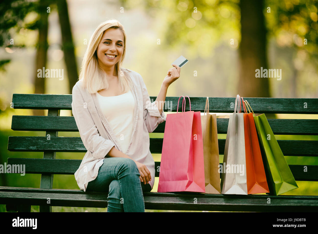 Junge glückliche Frau sitzen im Park nach Einkaufs- und Kreditkarte halten. Stockfoto