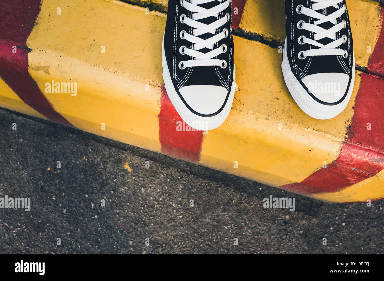 Schwarz / weiß neue Turnschuhe, Teenager Füße auf gelbe rote städtische Straße Grenze stehen. Nahaufnahme Foto mit selektiven Fokus Stockfoto