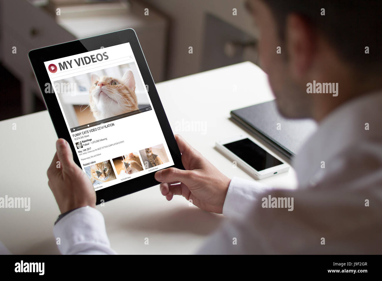 Bussinessman im Büro eine Tablette zeigt Katze Videos Website halten. Alle Bildschirm-Grafiken bestehen. Stockfoto