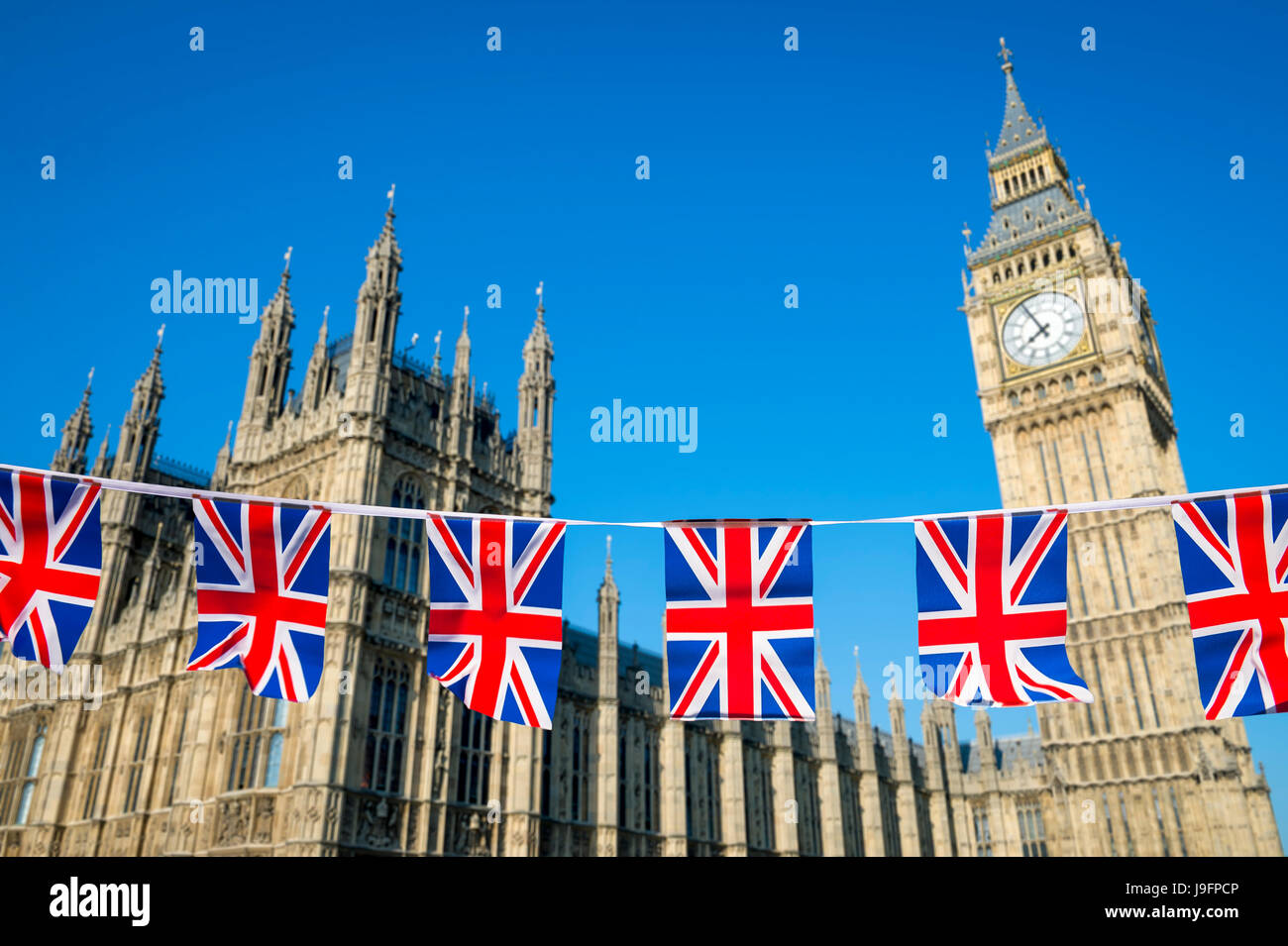 Union Jack Bunting fliegen vor den Houses of Parliament, Westminster Palace mit Big Ben unter strahlend blauem Himmel in London, England Stockfoto