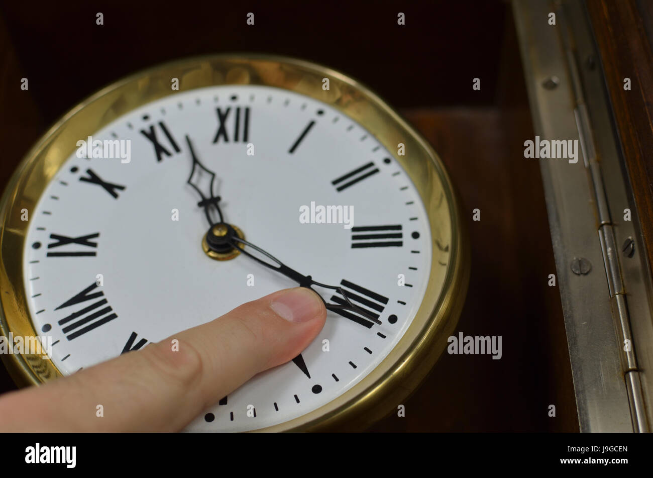 Ein Finger auf eine Seite einer Vintage Uhr versucht, ihn zu stoppen oder zu versuchen, die Zeit zurück drehen Stockfoto