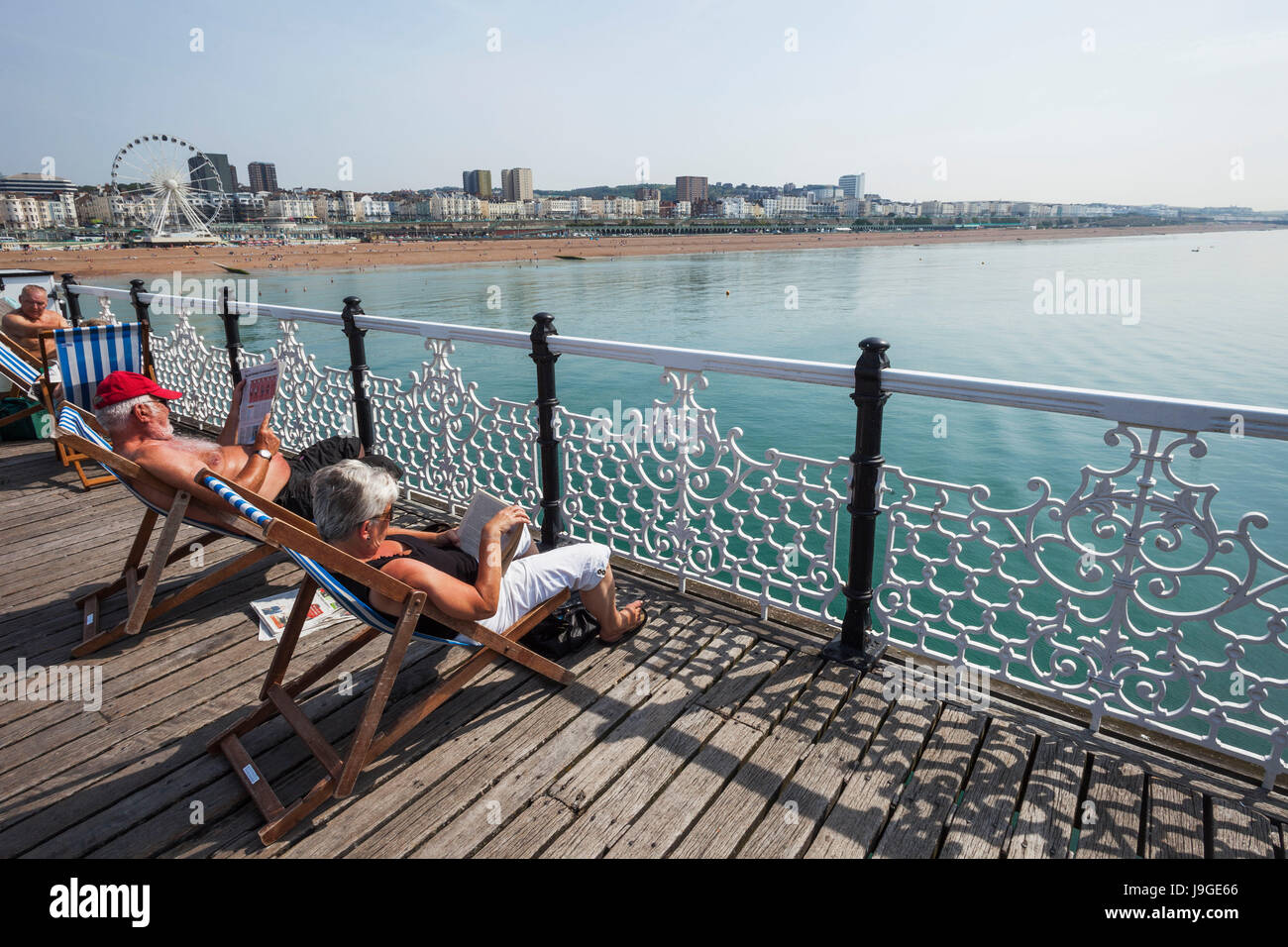 England, East Sussex, Brighton, Brighton Beach, Pier von Brighton, Leute sitzen auf den Liegestühlen, Stockfoto