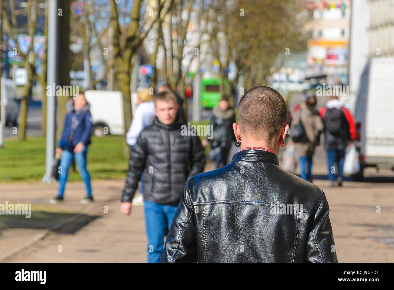 Minsk, Belarus - 22. April 2017: Ein junger Mann mit einem Kurzhaarschnitt und farbige Ohrringe in einer schwarzen Lederjacke geht weg. Blick von der Rückseite Stockfoto
