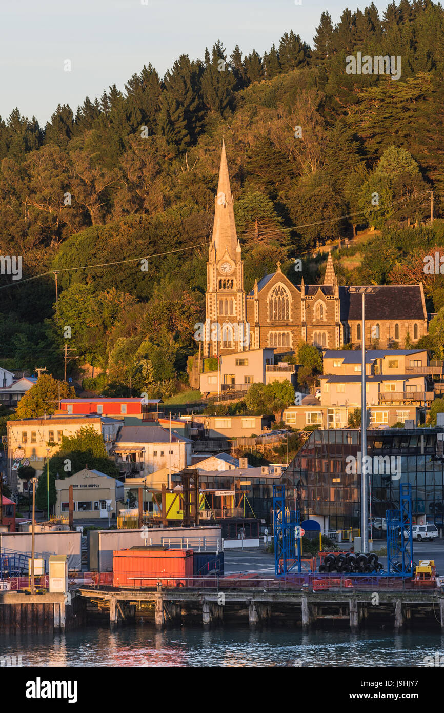 Port Chalmers, New Zealand - 15. März 2017: Iona Kirche unter Sonnenaufgang Licht erhebt sich über dem Hafen. Grün bewaldeten Hügel auf der Rückseite. Häuser, Verkehr und Stockfoto