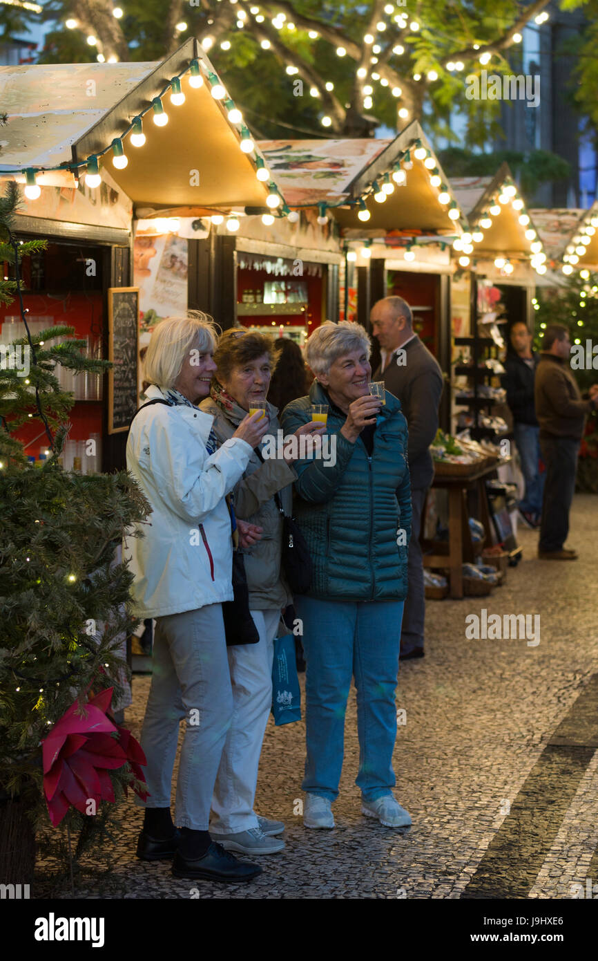 Drei Touristen trinken Punsch auf Funchals Avenida Arriaga Weihnachtsmarkt Stockfoto