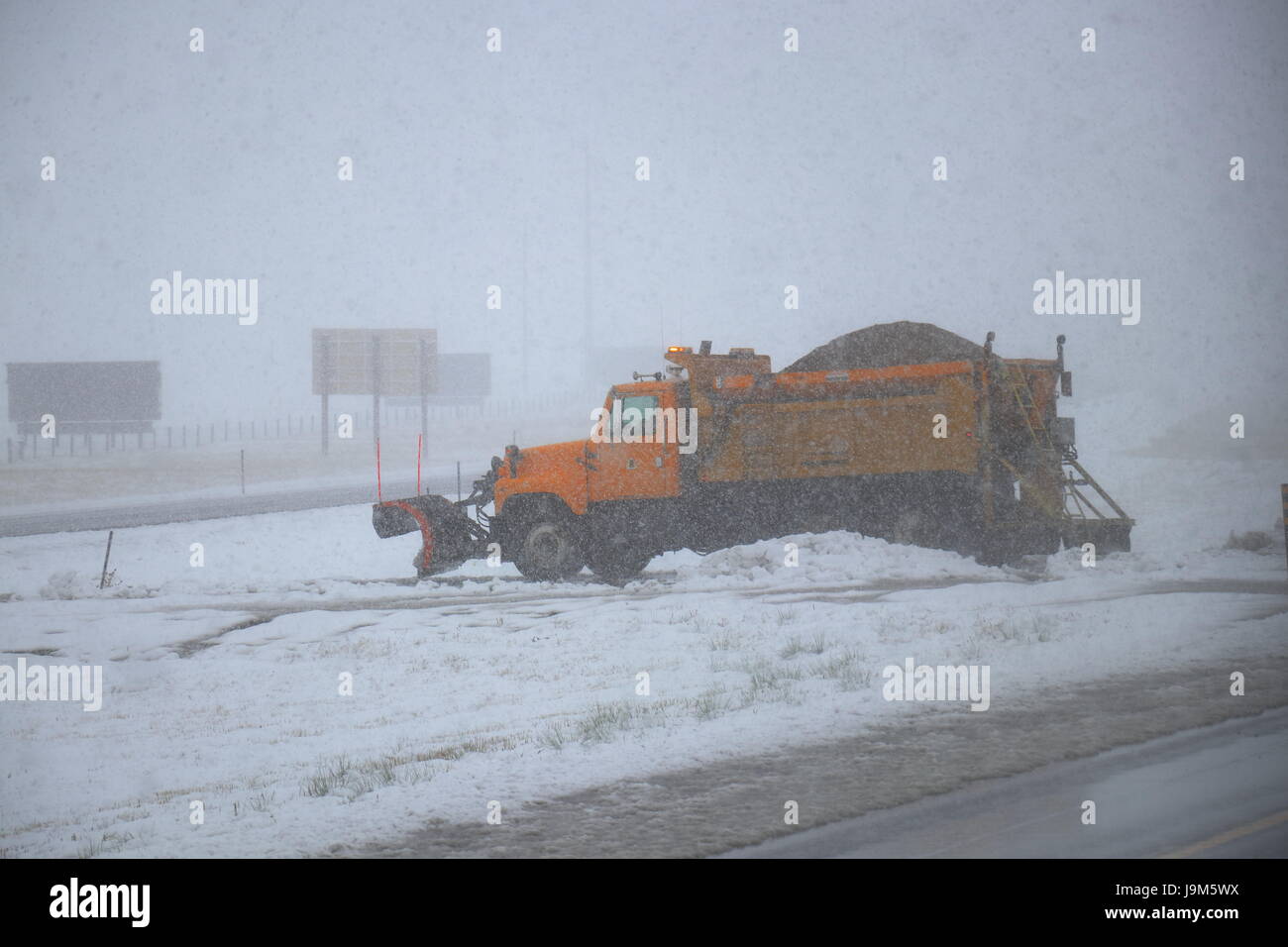Ein gelb/Orange Schneepflug geparkt in der Median der Interstate in Wyoming, USA. Stockfoto