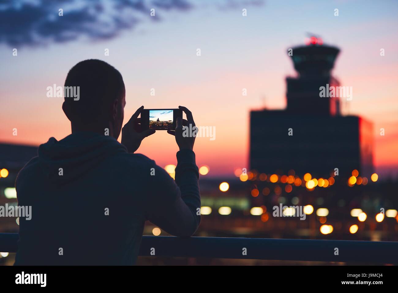 Silhouette des Reisenden mit Handy am Flughafen. Air Traffic Control Tower in den traumhaften Sonnenuntergang. Prag, Tschechische Republik. Stockfoto