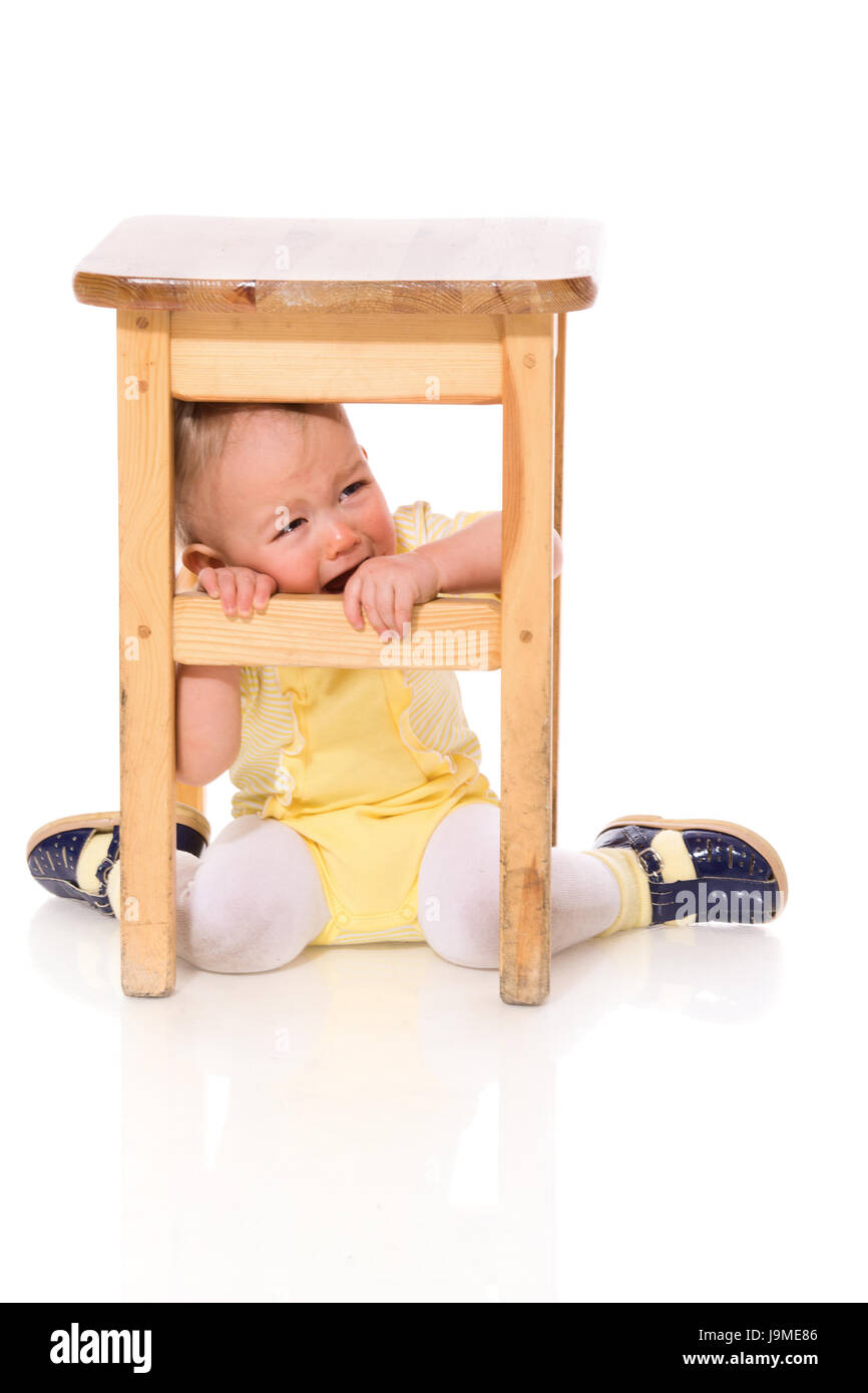 Säugling versteckt unter Stuhl Weinen isoliert auf weiss Stockfoto