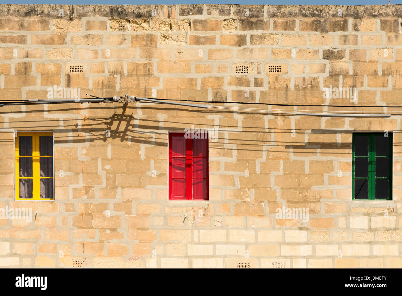 Drei bunte Fenster lackiert, gelb, rot und Grün in einem alten Steingebäude in Marsaxlokk Malta Stockfoto