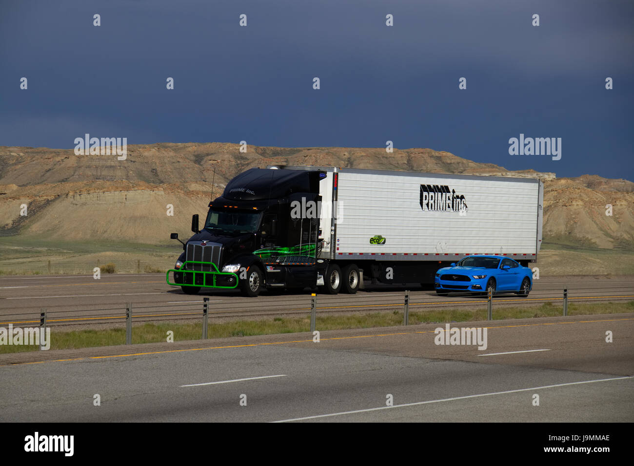 Ein schwarz Peterbilt semi-LKW ziehen einen weißen "Prime Inc." Trailer neben einem blauen Ford Mustang auf einem ländlichen US-Highway. Stockfoto