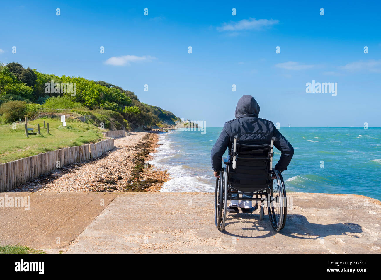 Deaktiviert allein jungen Mann in einem Rollstuhl sitzt und blickt auf das Meer. Stockfoto